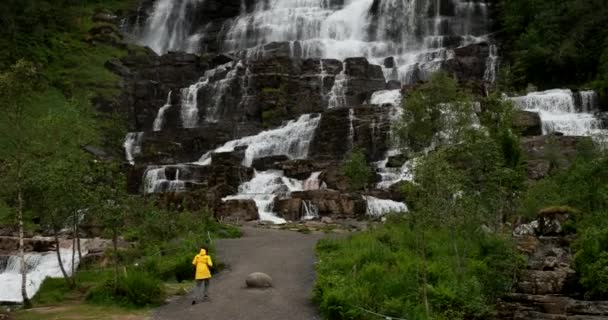 Восс, Хордаланд, Норвегия. Водопад Твиндефоссен весной. Молодая белая женщина-туристка, путешествующая по самому высокому водопаду Норвегии. Знаменитая норвежская достопримечательность и популярное направление — стоковое видео