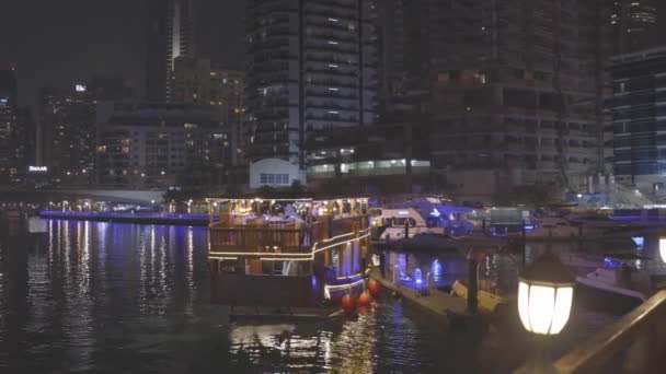 Порт Дубай Марина, Объединенные Арабские Эмираты - 19 мая 2021 года: лодка, прогулочный катер на Dubai Marina. Ночная прогулка возле Эйн-Дубая - самое большое колесо обозрения в мире, расположенное на — стоковое видео
