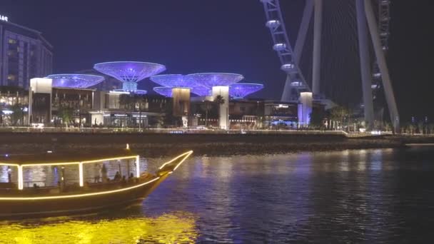 Порт Дубай Марина, Объединенные Арабские Эмираты - 19 мая 2021 года: лодка, прогулочный катер на Dubai Marina. Ночная прогулка возле Эйн-Дубая - самое большое колесо обозрения в мире, расположенное на — стоковое видео