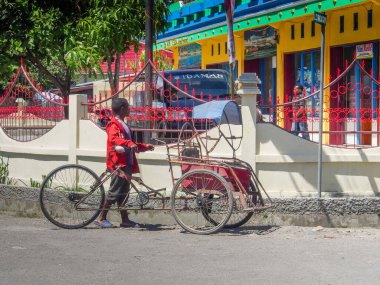 Wamena, Indonesia - January 23, 2015: A rickshaw driver. Young, dark skin boy waiting for a client on the street of Wamena