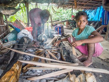 Jungle, Endonezya - 13 Ocak 2015: Korowai kabilesinden iki kız ahşap evin içindeki şöminenin üzerinde yemek hazırlıyor. Batı Papua, Endonezya