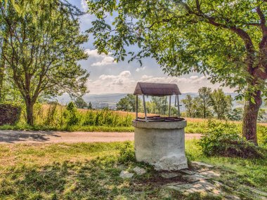 Old, stone, water well  with a windlass and crank in the polish village and view of the Cergowa Hill in the Low Beskids, Beskid Niski, Poland clipart
