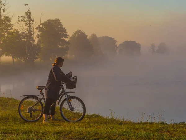 A woman with bicycle  during the foggy morning. Bug River.  Podlasie. Podlachia. Poland, Europe. The region is called Podlasko or Podlasze. Panoramic view.