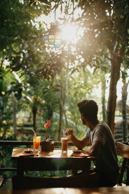 Genç adam masada oturuyor ve kahve içiyor.