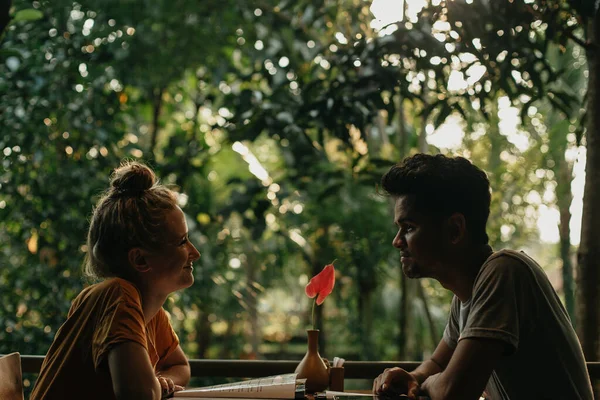 Young interracial couple looking at each other at a forest cafe table