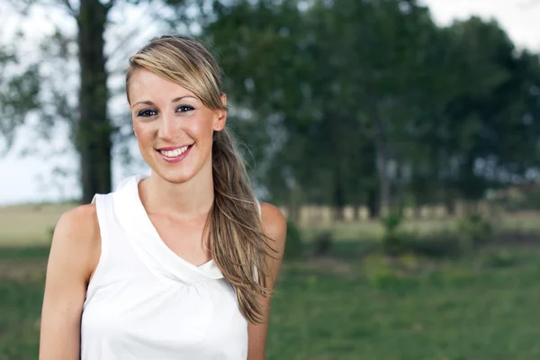 Happy woman posing in the field on a background of trees — Stock Photo, Image