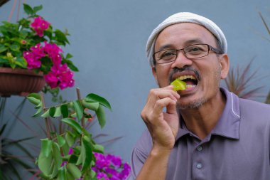 Bahçede taze yıldız meyvesi yiyen bir adam.