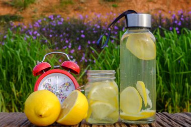 Tazelik kavramı. Limonata, çalar saat ve ahşap arka planda kavanozda limon dilimleri. Kapat..