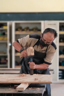 Marangoz atölyede ahşap işçiliği üzerine çalışarak inşaat malzemesi veya ahşap mobilya üretiyor.