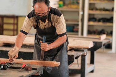 Marangoz atölyede ahşap işçiliği üzerine çalışarak inşaat malzemesi veya ahşap mobilya üretiyor.