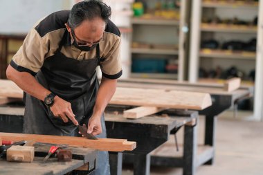 Marangoz atölyede ahşap işçiliği üzerine çalışarak inşaat malzemesi veya ahşap mobilya üretiyor.
