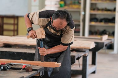 Marangoz atölyede ahşap işçiliği üzerine çalışarak inşaat malzemesi veya ahşap mobilya üretiyor.