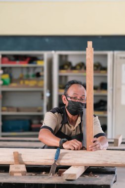Marangoz atölyede ahşap işçiliği üzerine çalışarak inşaat malzemesi veya ahşap mobilya üretiyor.