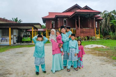 Batu Pahat, Malezya - 3 Mayıs 2022: Geleneksel kıyafetler içinde mutlu Malay ailesi ve Hari Raya sırasındaki geleneksel Malay evi. Malezya aile yaşam tarzı evde. Mutluluk kavramı.