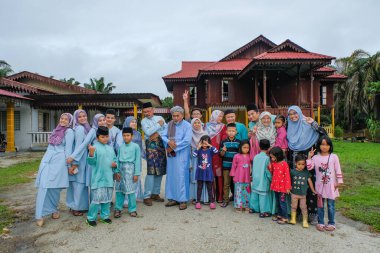 Batu Pahat, Malezya - 3 Mayıs 2022: Geleneksel kıyafetler içinde mutlu Malay ailesi ve Hari Raya sırasındaki geleneksel Malay evi. Malezya aile yaşam tarzı evde. Mutluluk kavramı.