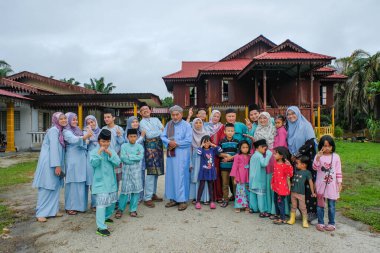 Batu Pahat, Malezya - 3 Mayıs 2022: Geleneksel kıyafetler içinde mutlu Malay ailesi ve Hari Raya sırasındaki geleneksel Malay evi. Malezya aile yaşam tarzı evde. Mutluluk kavramı.