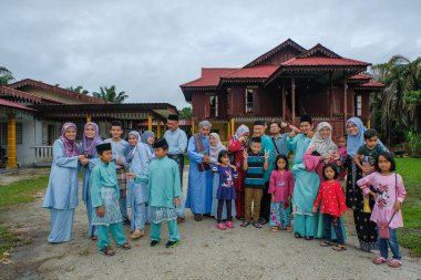 Batu Pahat, Malezya - 3 Mayıs 2022: Geleneksel kıyafetler içinde mutlu Malay ailesi ve Hari Raya sırasındaki geleneksel Malay evi. Malezya aile yaşam tarzı evde. Mutluluk kavramı.