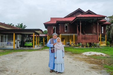 Batu Pahat, Malezya - 3 Mayıs 2022: Geleneksel kıyafetler içinde mutlu Malay ailesi ve Hari Raya sırasındaki geleneksel Malay evi. Malezya aile yaşam tarzı evde. Mutluluk kavramı.
