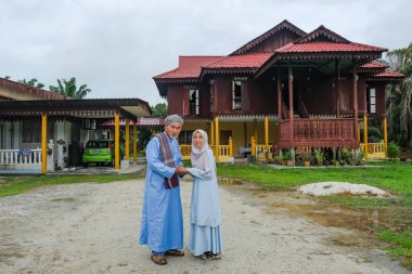 Batu Pahat, Malezya - 3 Mayıs 2022: Geleneksel kıyafetler içinde mutlu Malay ailesi ve Hari Raya sırasındaki geleneksel Malay evi. Malezya aile yaşam tarzı evde. Mutluluk kavramı.