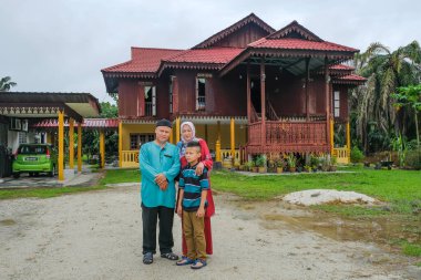 Batu Pahat, Malezya - 3 Mayıs 2022: Geleneksel kıyafetler içinde mutlu Malay ailesi ve Hari Raya sırasındaki geleneksel Malay evi. Malezya aile yaşam tarzı evde. Mutluluk kavramı.