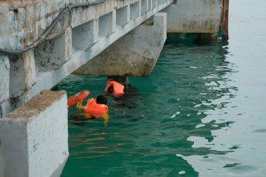 Tioman, Malezya - 20 Nisan 2022: İnşaat işçisi beton bir iskeleyi onarmak için deniz suyunun üzerinde yapı iskelesi kuruyor.