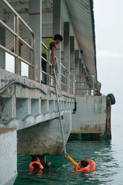 Tioman, Malezya - 20 Nisan 2022: İnşaat işçisi beton bir iskeleyi onarmak için deniz suyunun üzerinde yapı iskelesi kuruyor.