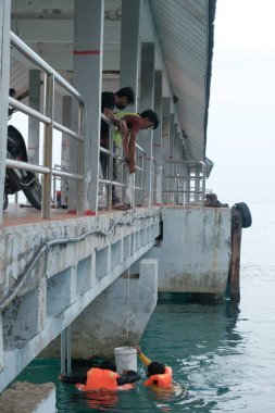 Tioman, Malezya - 20 Nisan 2022: İnşaat işçisi beton bir iskeleyi onarmak için deniz suyunun üzerinde yapı iskelesi kuruyor.