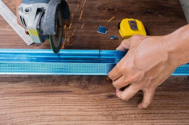Worker using grinding machine to cut steel roof batten.