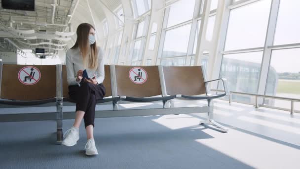 Confident business woman in a mask sitting at the airport, holding a passport and plane tickets, keeps a distance in a pandemic. Waiting at the airport. Pandemic travel concept. Social distance — Stock Video