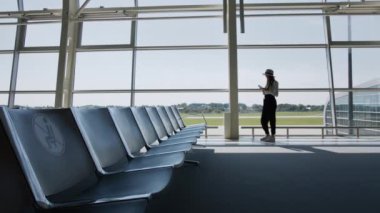 Kadın gezgin, boş zaman ve iş yeri büyük uluslararası bir havaalanı merkezinin cam penceresinde elinde telefonla akıllı telefonlar için başvuru formunu sarıyorum. Biletlerin ellerinde.