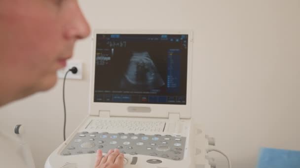 Kocasıyla ilgilenen hamile kadın, düzenli teşhis için kliniğe gidiyor. Uzman jinekolog hasta için ultrason taraması yapıyor. Hamilelik, destek ve sağlık hizmetleri kavramı. — Stok video