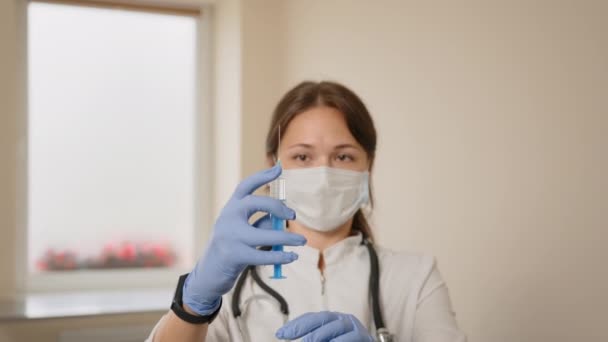 Bij een close-up van een vrouwelijke arts met een medisch masker die een insulinespuit vasthoudt, komt er lucht vrij uit de spuit. Inenting. — Stockvideo