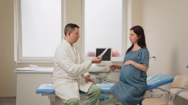 Médecin montrant des images après échographie à la femme enceinte — Video