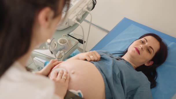 Vista dall'alto di una bella donna incinta sdraiata sul divano medico mentre il ginecologo competente esamina il battito cardiaco del bambino. Attrezzature moderne per il check up. Assistenza sanitaria durante la gravidanza. — Video Stock