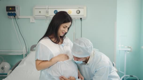 Echtgenoot omarmt zachtjes buik van zwangere vrouw in kliniek — Stockvideo