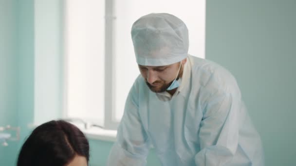 Fürsorglicher Ehemann in medizinischer Kleidung massiert Schwangeren, die auf einem Fitnessball sitzen, den Rücken. Kaukasische Frau bekommt bei Bauarbeiten in Klinik Unterstützung von Mann. — Stockvideo