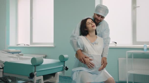 Grossesse caucasienne ressentant une forte douleur pendant les contractions à l'hôpital. mari attentionné en vêtements médicaux debout derrière et massant son dos. Concept de soutien et d'amour. — Video