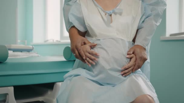 Kaukasische Schwangere verspürt starke Schmerzen während der Wehen auf der Krankenhausstation. Fürsorglicher Ehemann in medizinischer Kleidung, der hinter ihr steht und ihr den Rücken massiert. Unterstützungs- und Liebeskonzept — Stockvideo