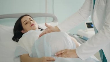 Profesyonel jinekolog karnını muayene ederken hamile bir kadın tıbbi kanepede yatıyor. Modern klinikte doğum öncesi kadın hastayı muayene eden kadın doktor..