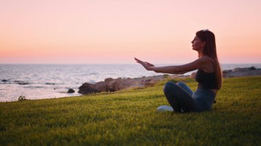 Huzurlu bir kadın akşam vakti sahilde meditasyon yapıyor.
