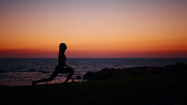 Donna attiva stretching corpo durante il tramonto sull'oceano — Foto Stock