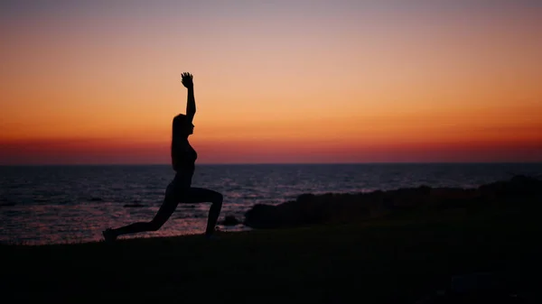 Donna attiva stretching corpo durante il tramonto sull'oceano — Foto Stock
