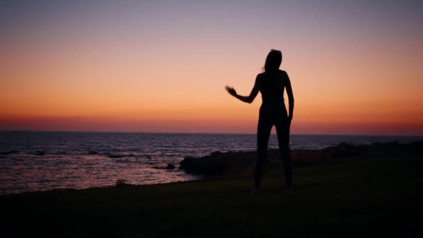 Mujer joven con cuerpo delgado practicando ejercicios de fitness durante la noche cerca del océano. Silueta de mujer activa y saludable. Entrenamiento regular para el cuidado del cuerpo. Mujer fitness cerca del océano — Vídeos de Stock