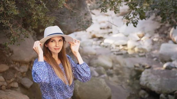 Portrait, Charming caucasian woman wearing summer hat and clothes walking among high rocks and looking around. Female tourist discovering new place during summer adventure. Charming woman in summer