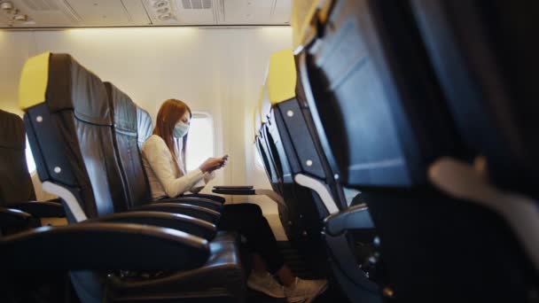 Деловая женщина в маске с помощью мобильного в самолете — стоковое видео