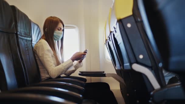 Mujer con máscara facial usando smartphone durante el vuelo de negocios — Vídeos de Stock