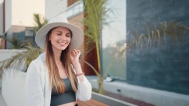 Şık giyinmiş, yaz şapkalı, gülen genç bir kadın palmiye ağaçlarının arasında dikilirken selfie çekmek için modern akıllı telefonu kullanıyor. Teknoloji ve yolculuk kavramı. Mutlu kadın selfie çekiyor.