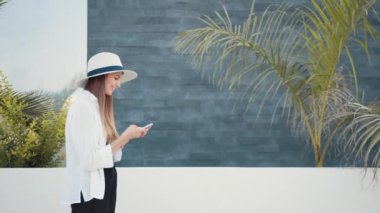 Yazlık şapkalı gülümseyen kadın açık havada cep telefonu kullanıyor.