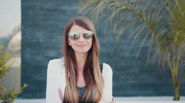 Güneş gözlüklü kadın sokakta durup gülümsüyor.