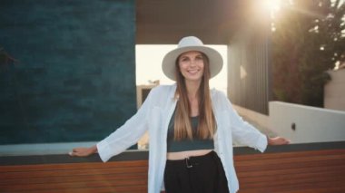 Şık yaz elbiseleri ve çitin yanında poz veren şapkalı bir kadın.